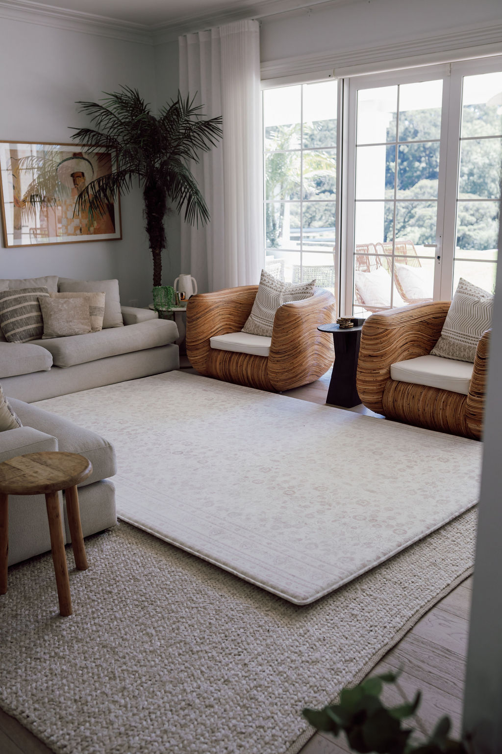Modern living room with a Toffee Play Rug by Little Wiwa, cream sofa, wicker chairs, and large windows.